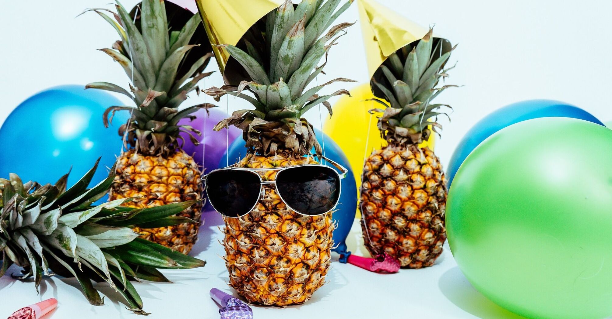 A pineapple with sunglasses surrounded by colorful balloons and party favors, suggesting a festive or celebratory mood