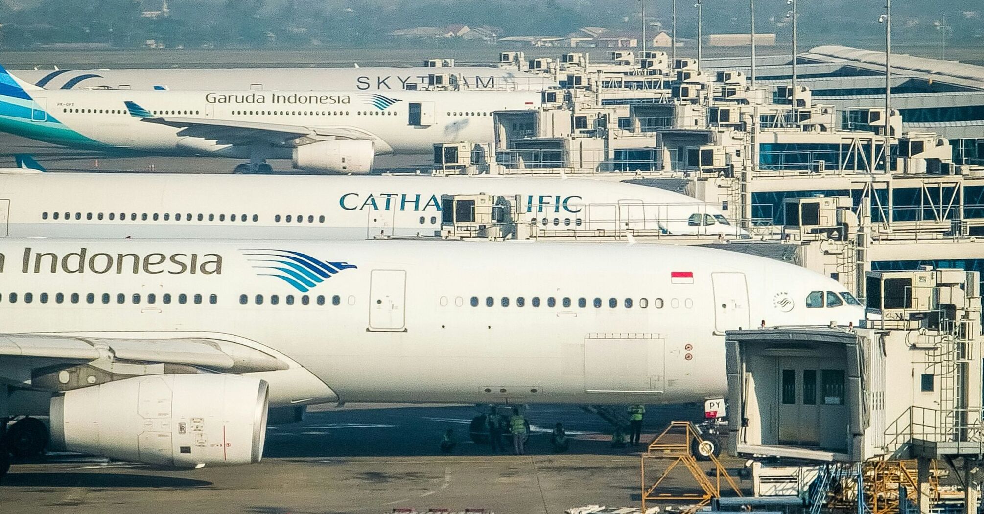 Commercial airplanes from various airlines parked at airport gates with jet bridges and ground service equipment visible