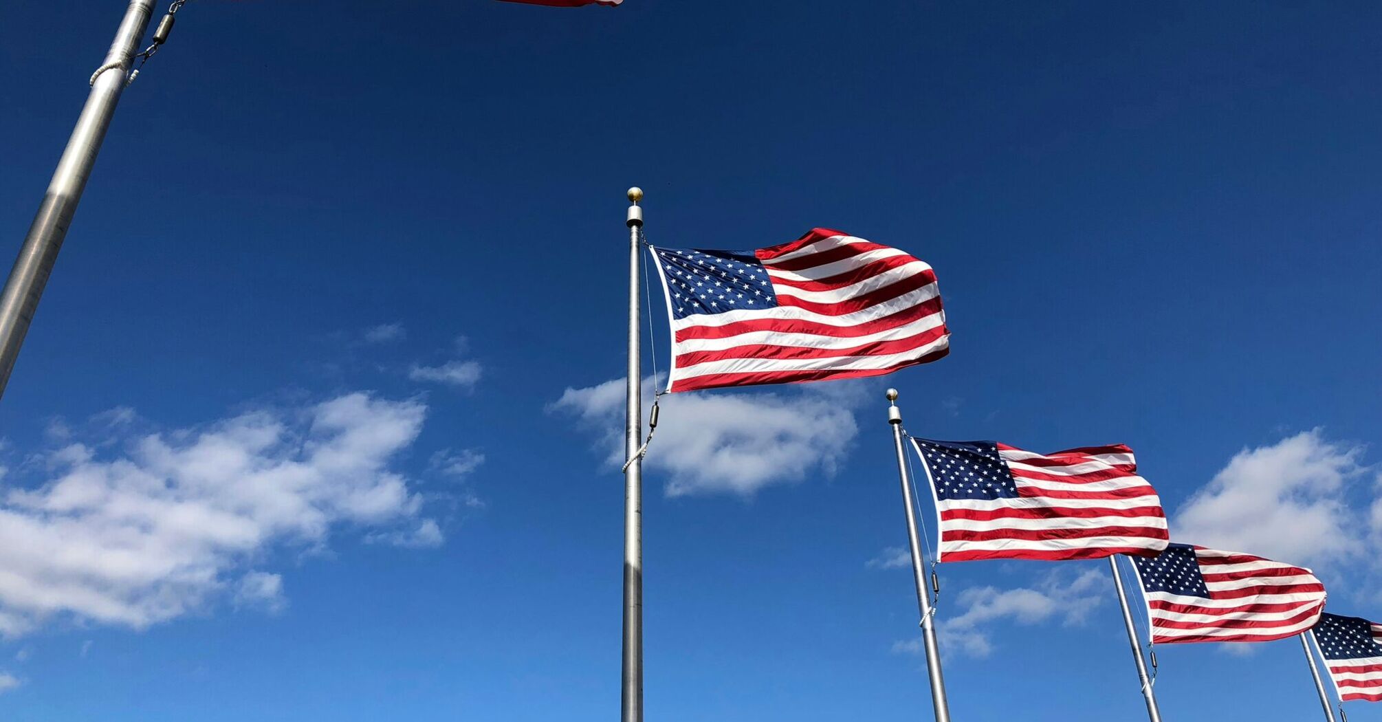 Multiple American flags on flagpoles against a blue sky with scattered clouds