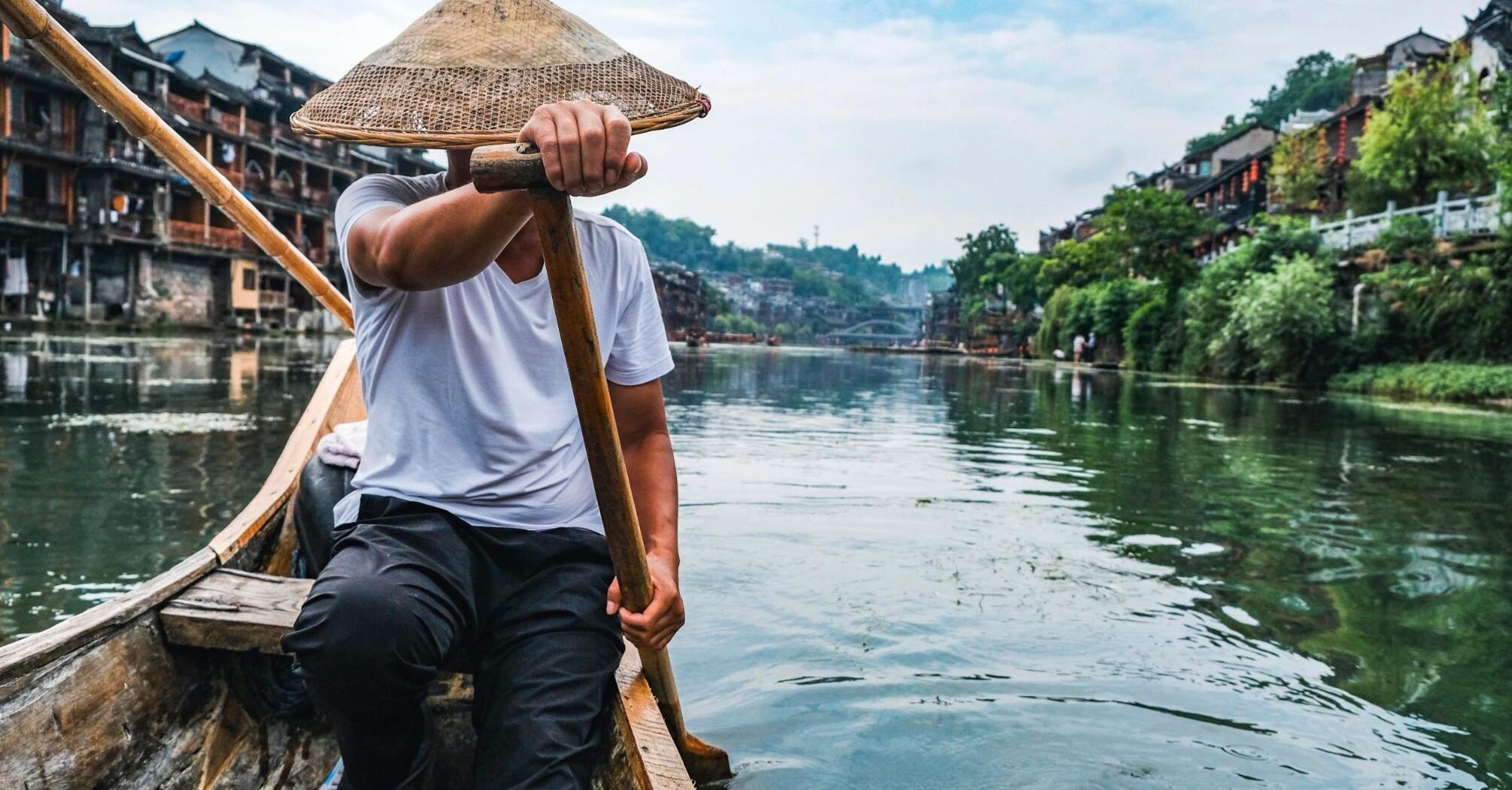 A man navigating a traditional wooden boat on a river in a historic Chinese town