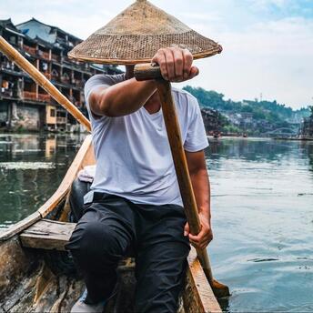 A man navigating a traditional wooden boat on a river in a historic Chinese town