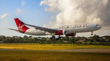 Virgin Atlantic aircraft landing on a runway with greenery in the background under a partly cloudy sky