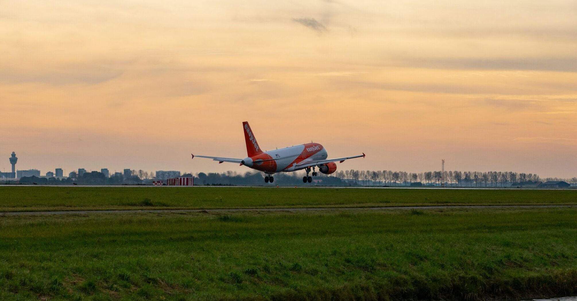 An easyJet plane taking off at sunset near a city