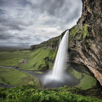 A breathtaking waterfall cascading over a lush green cliff in Iceland under a cloudy sky