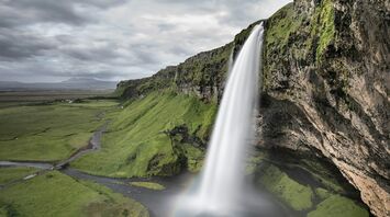 A breathtaking waterfall cascading over a lush green cliff in Iceland under a cloudy sky