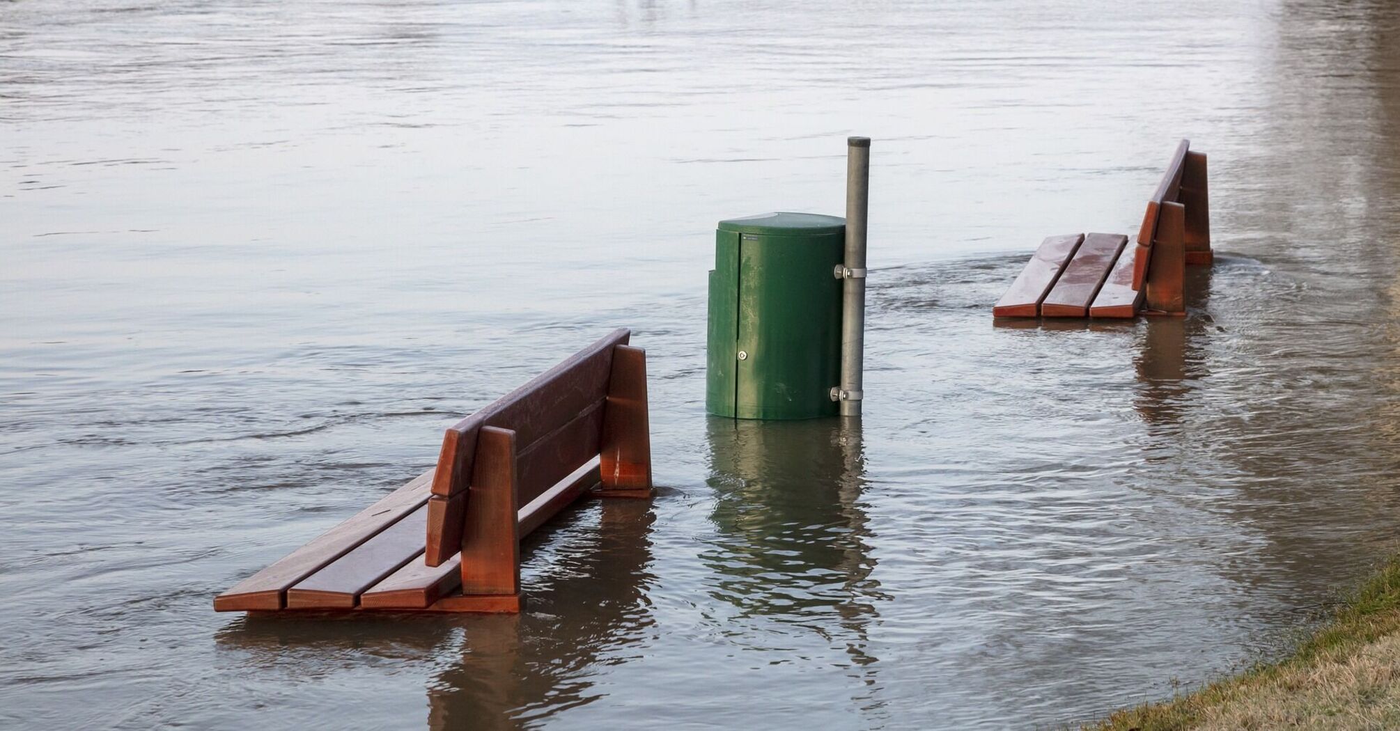 Flooded park benches submerged in water near a riverbank