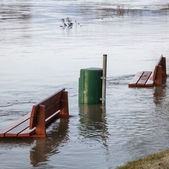 Flooded park benches submerged in water near a riverbank