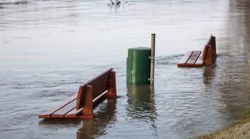 Flooded park benches submerged in water near a riverbank
