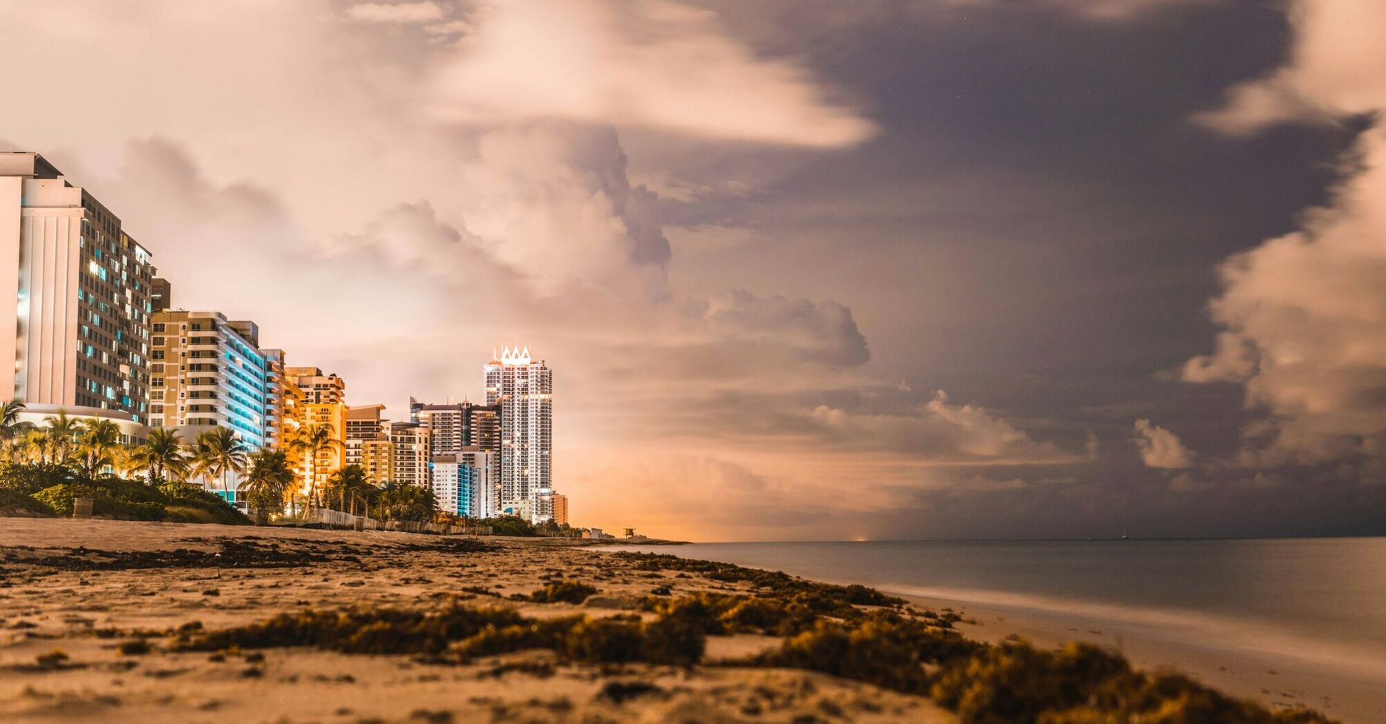 Night view of beachfront skyscrapers under a cloudy sky