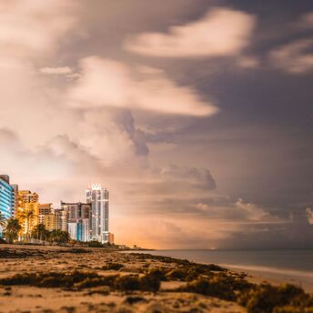 Night view of beachfront skyscrapers under a cloudy sky