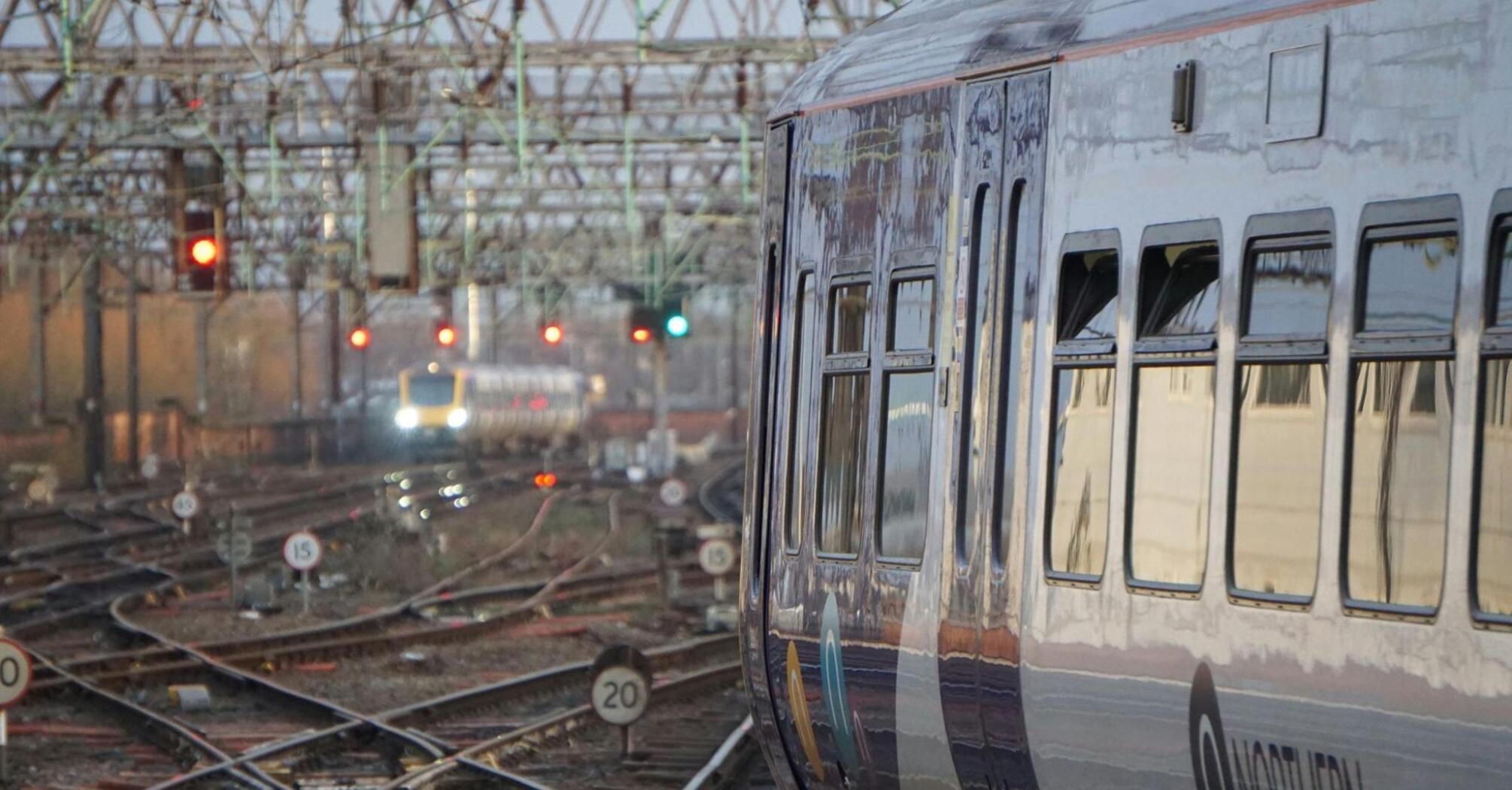 A train on a railway track with complex overhead wiring and signals at a busy junction