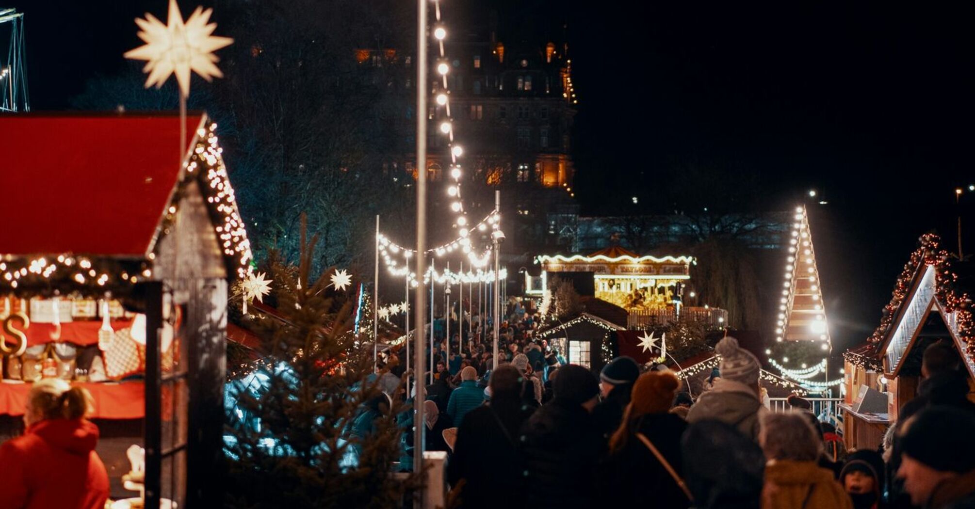 Crowded festive market stalls under string lights at night, with visitors enjoying the holiday atmosphere