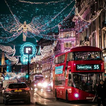 London’s Oxford Circus decorated with festive Christmas lights, featuring red double-decker buses and bustling evening traffic
