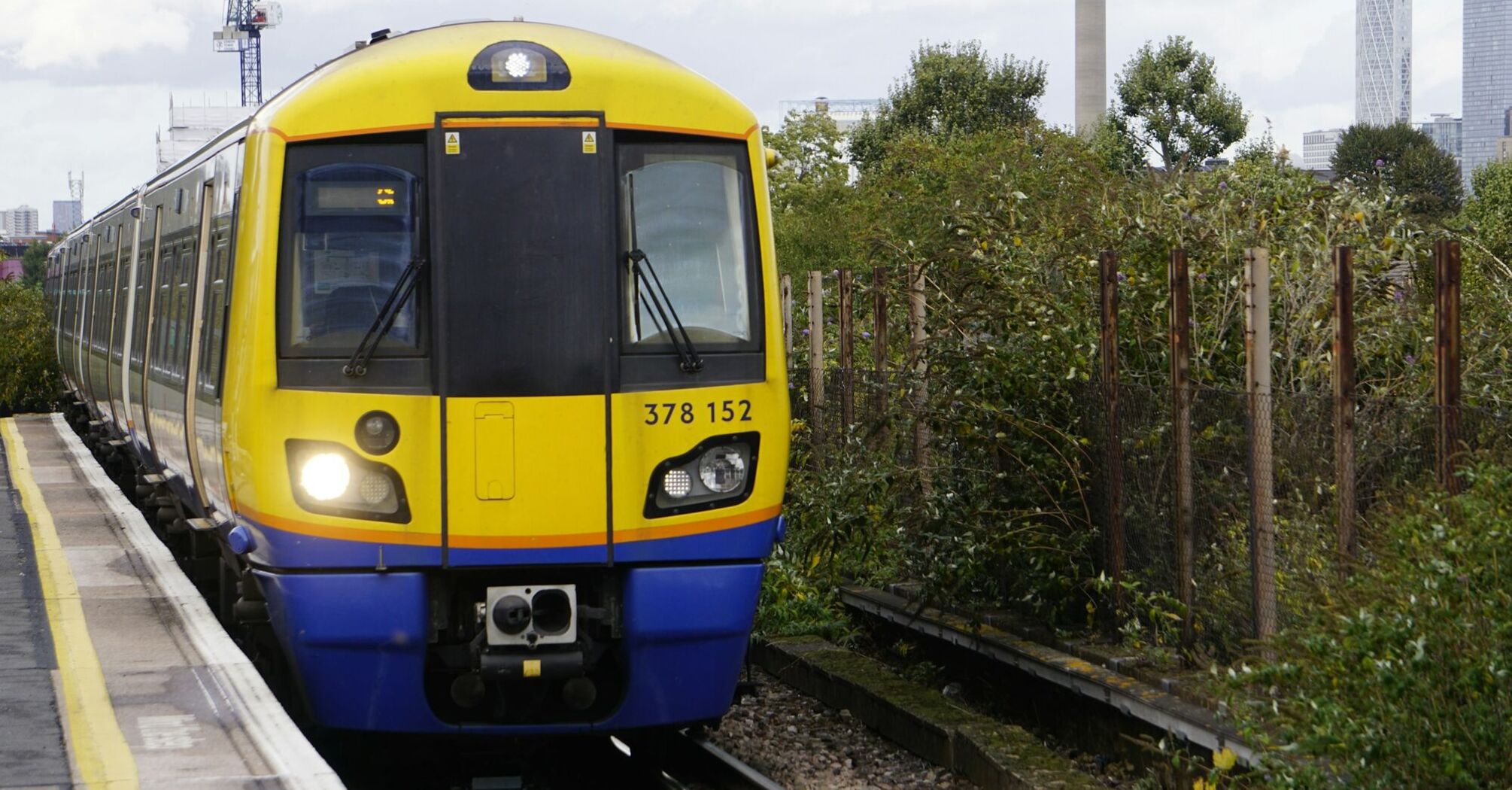 A yellow and blue London Overground train approaches a station platform