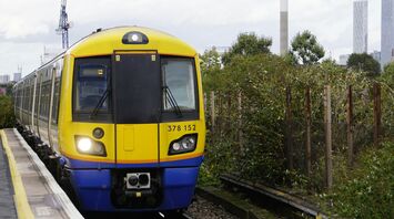 A yellow and blue London Overground train approaches a station platform