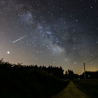 A meteor streaks across a star-filled night sky over a rural road
