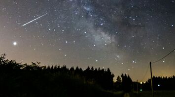 A meteor streaks across a star-filled night sky over a rural road