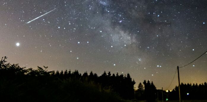 A meteor streaks across a star-filled night sky over a rural road