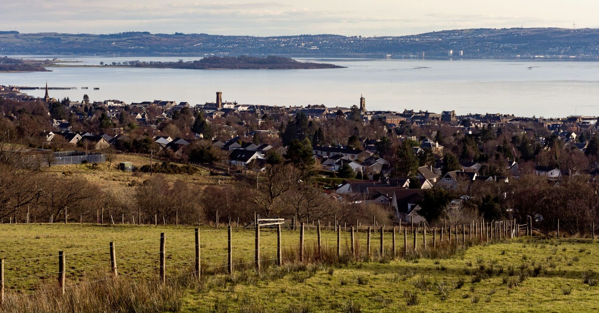 A scenic view of a coastal town with hills and water in the background, showcasing the serene landscape of West Scotland