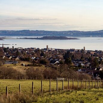 A scenic view of a coastal town with hills and water in the background, showcasing the serene landscape of West Scotland