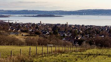 A scenic view of a coastal town with hills and water in the background, showcasing the serene landscape of West Scotland