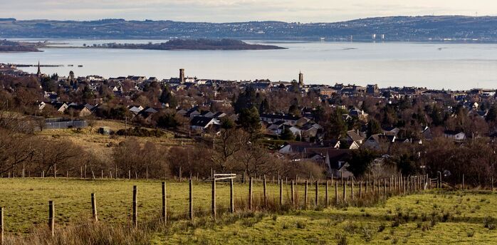 A scenic view of a coastal town with hills and water in the background, showcasing the serene landscape of West Scotland