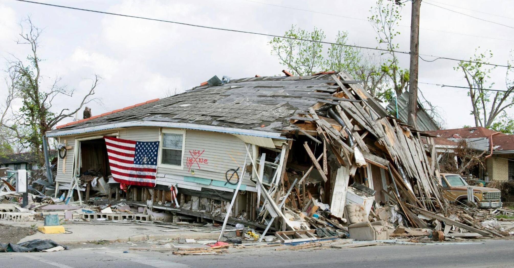 A house severely damaged by the hurricane, with a collapsed roof and an American flag on the front 