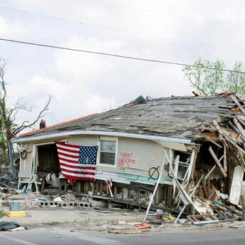 A house severely damaged by the hurricane, with a collapsed roof and an American flag on the front