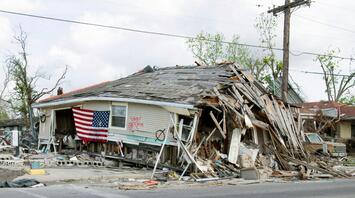 A house severely damaged by the hurricane, with a collapsed roof and an American flag on the front