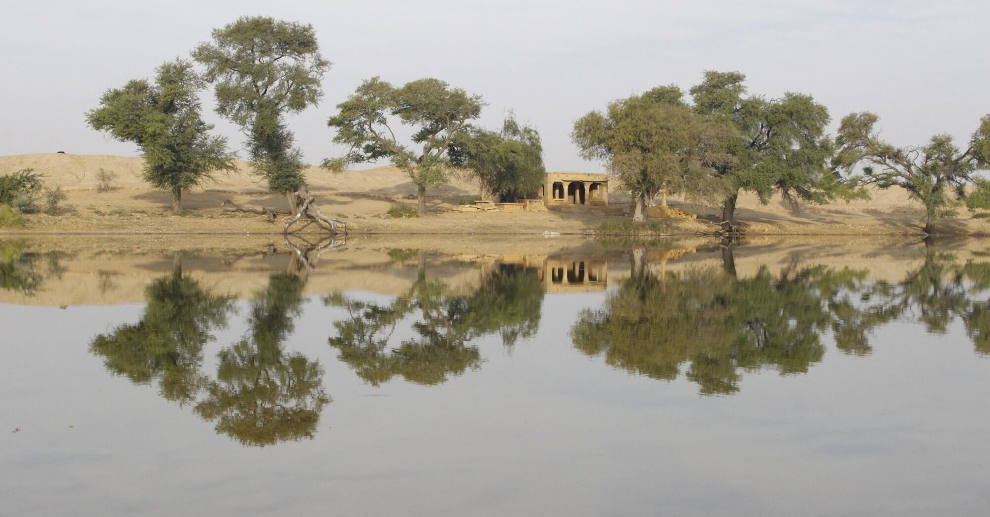 A calm desert lake reflecting trees and an old structure