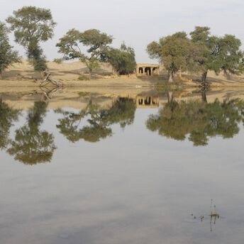A calm desert lake reflecting trees and an old structure