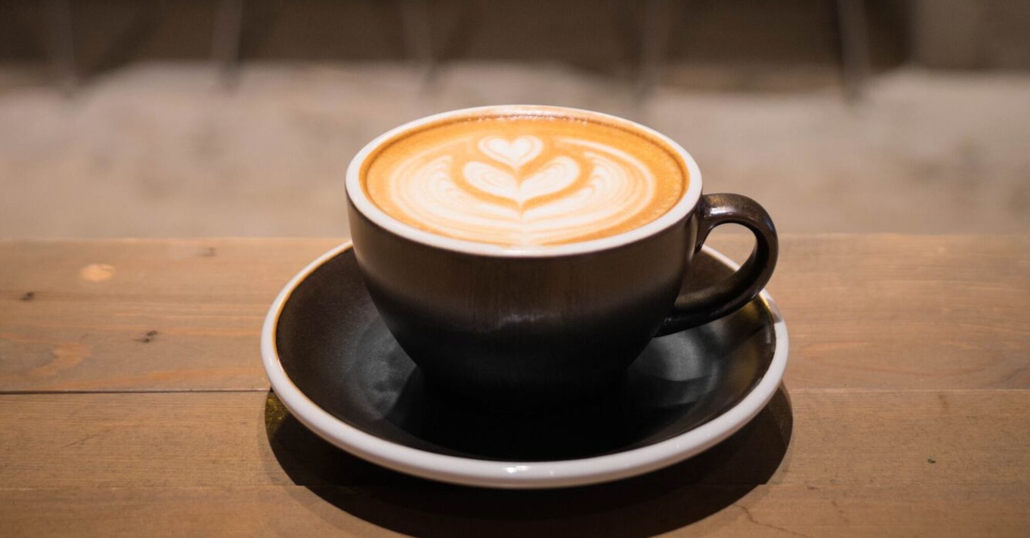 A cup of latte with heart-shaped foam art on a wooden table in a cafe