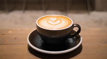 A cup of latte with heart-shaped foam art on a wooden table in a cafe
