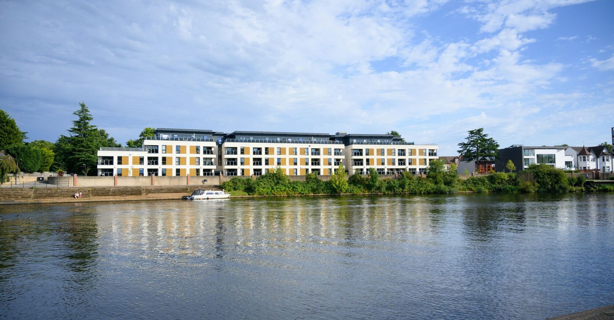 A view of modern riverside apartments next to the River Trent, reflecting on the water under a clear sky