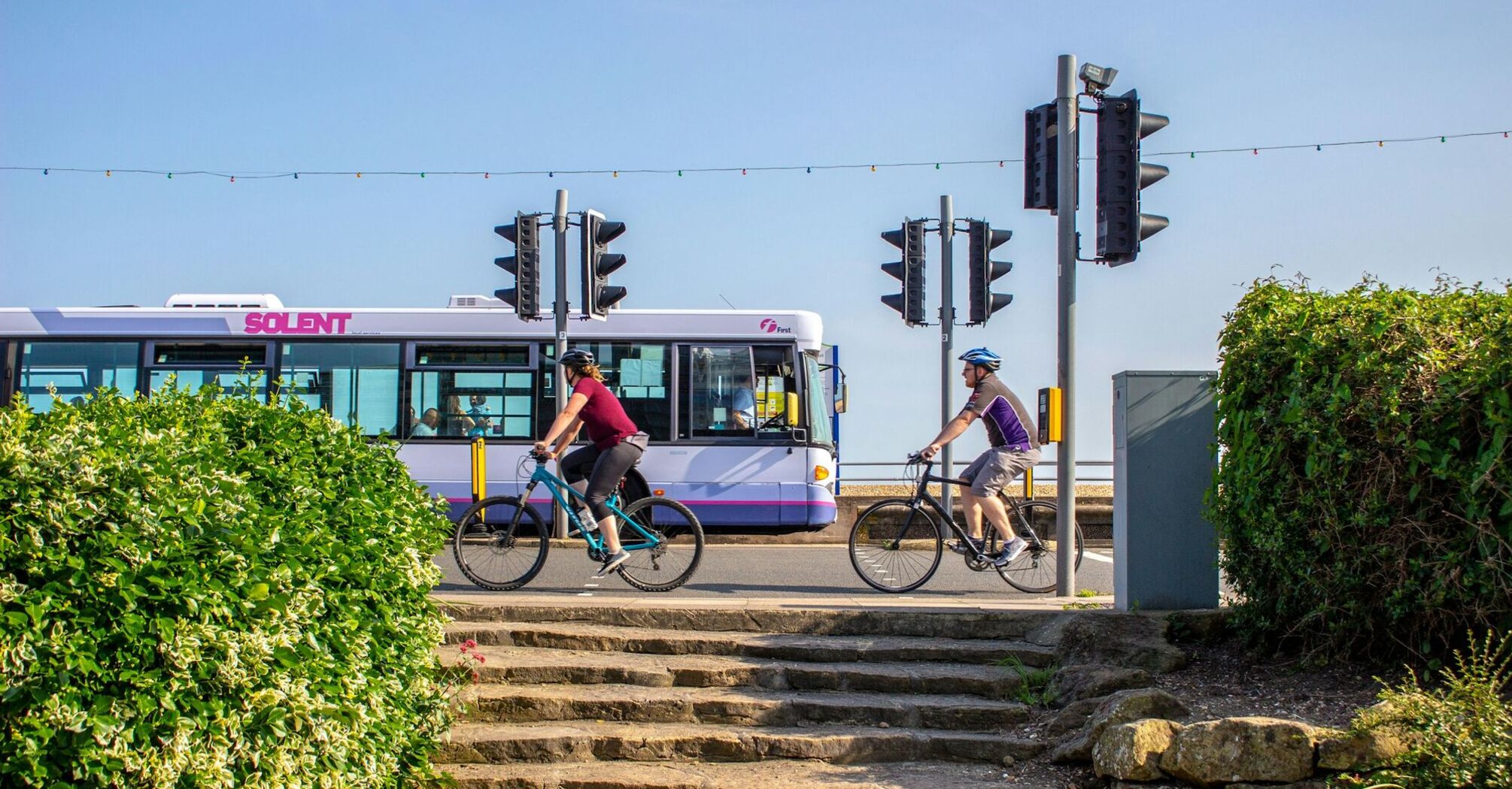 Cyclists riding past a Solent bus at a traffic signal on a sunny day in Portsmouth