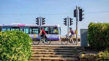 Cyclists riding past a Solent bus at a traffic signal on a sunny day in Portsmouth