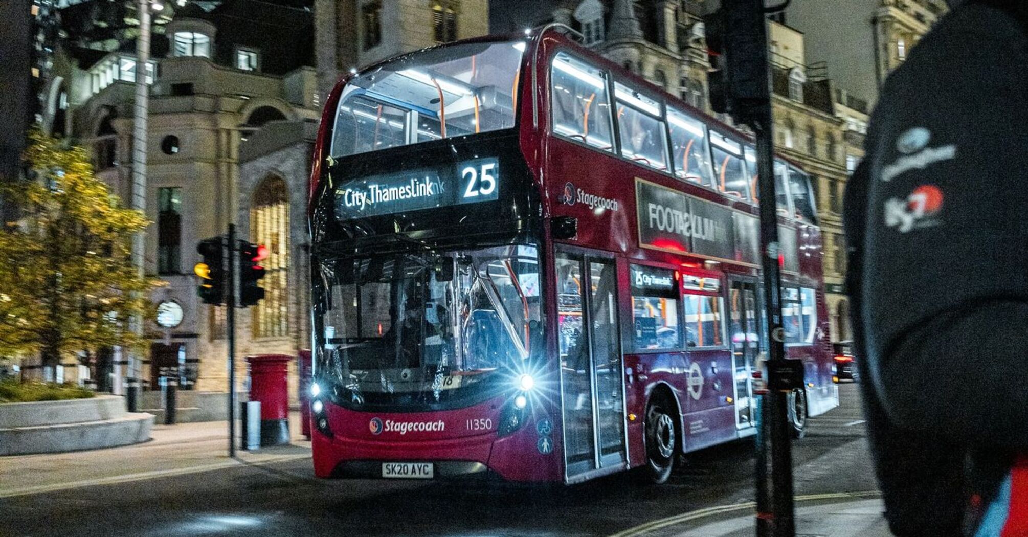 A red Stagecoach double-decker bus driving through the city at night, with London's Gherkin building in the background