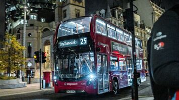 A red Stagecoach double-decker bus driving through the city at night, with London's Gherkin building in the background