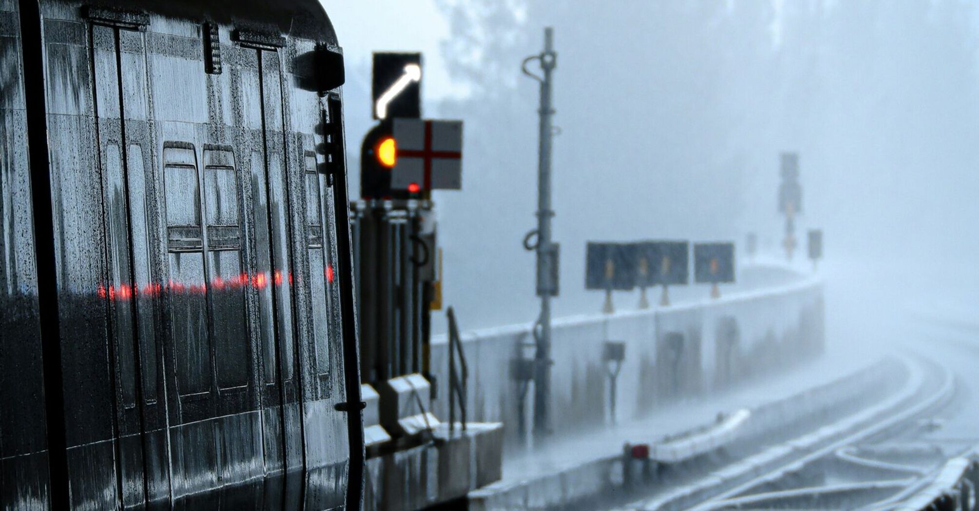 A train at a station platform during heavy rainfall, with misty conditions and water-covered tracks