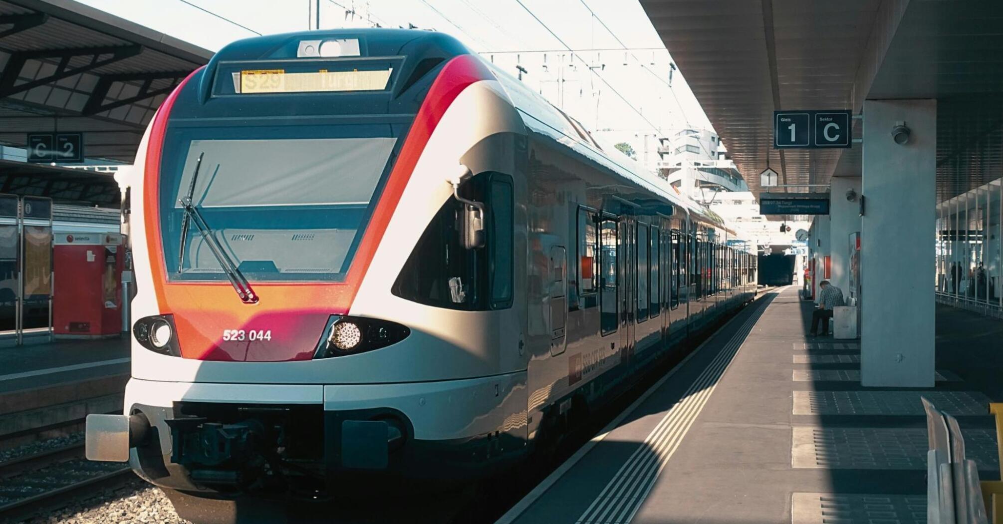 A modern European train waits at a station platform, bathed in sunlight, ready for departure