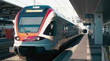 A modern European train waits at a station platform, bathed in sunlight, ready for departure