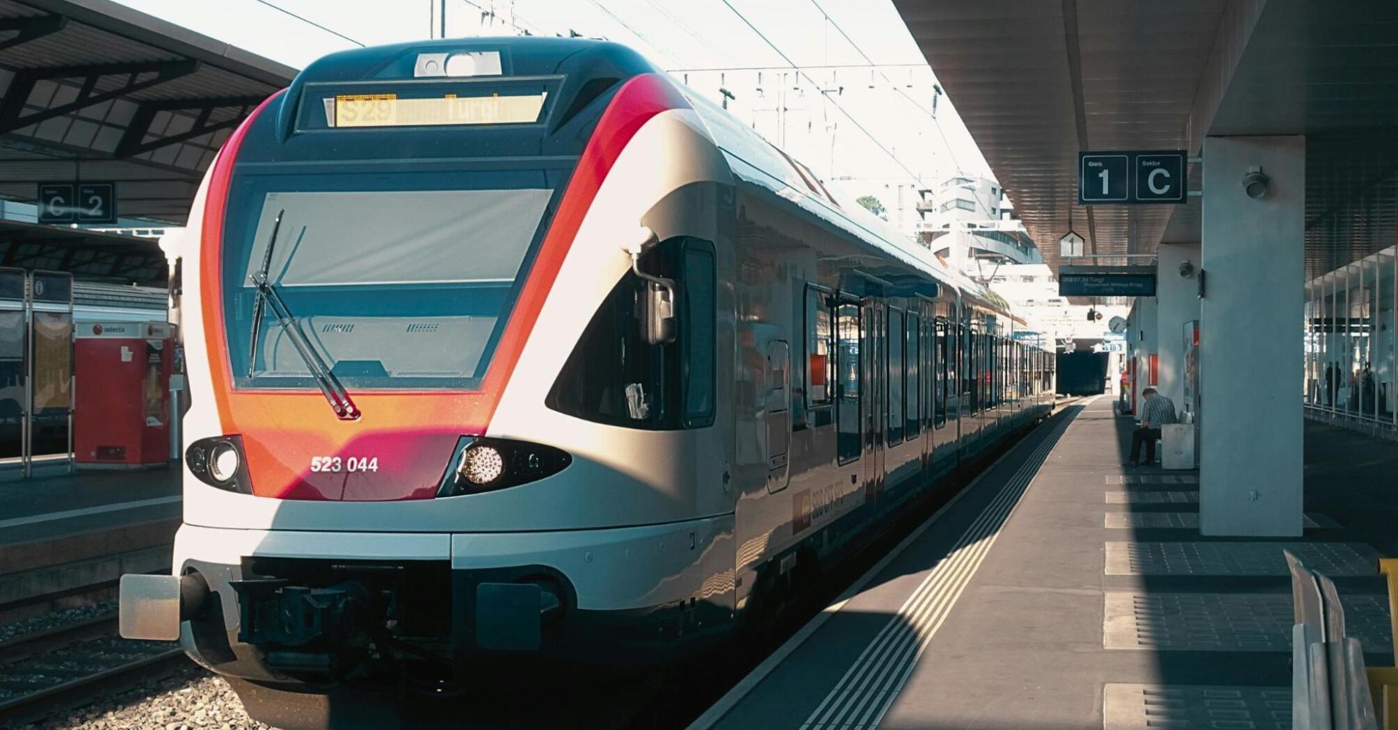 A modern European train waits at a station platform, bathed in sunlight, ready for departure