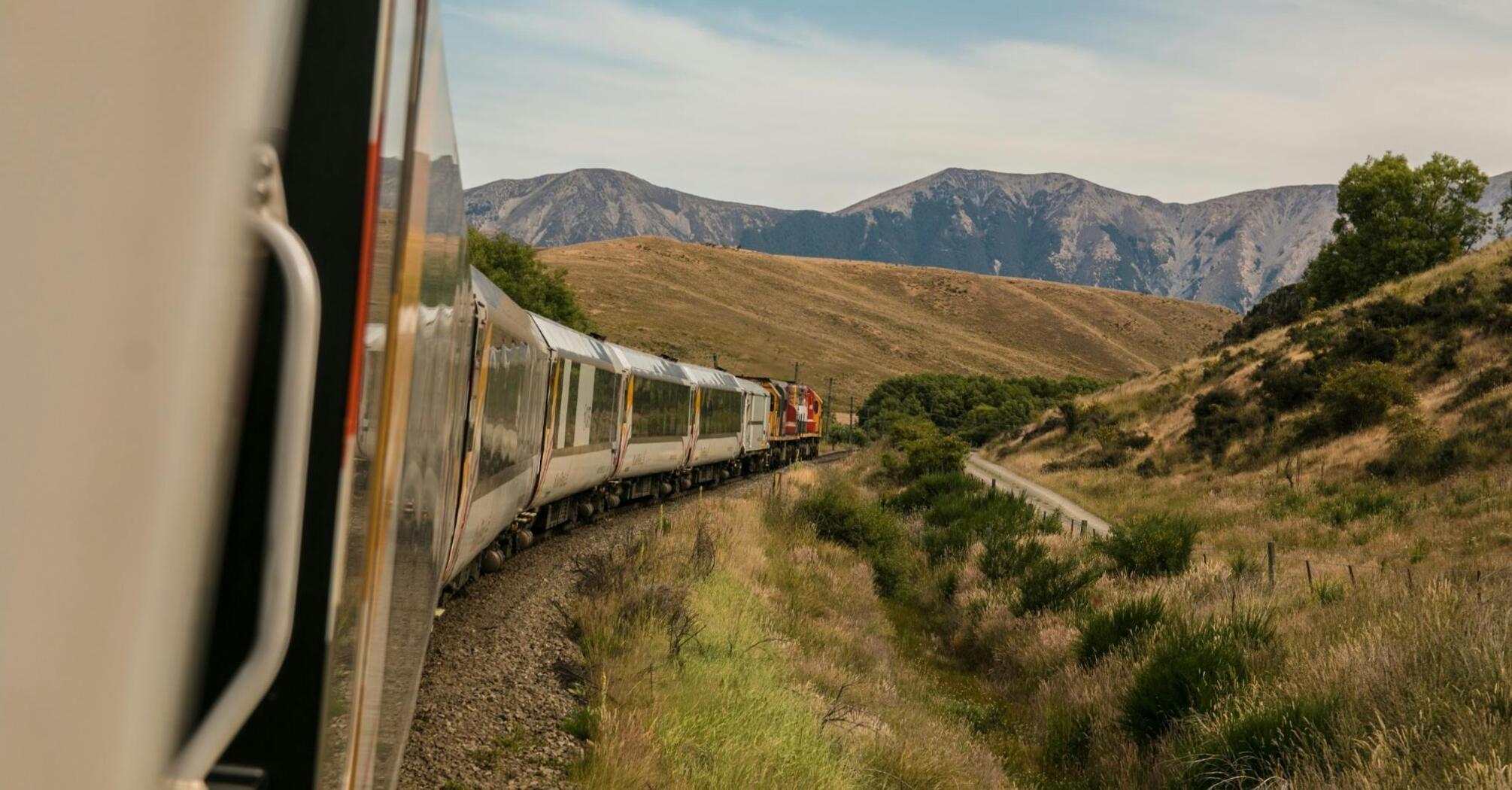 Train curving through a mountainous landscape with a view of hills and sparse vegetation