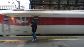 A traveler waits on a platform as an LNER train speeds past at a station
