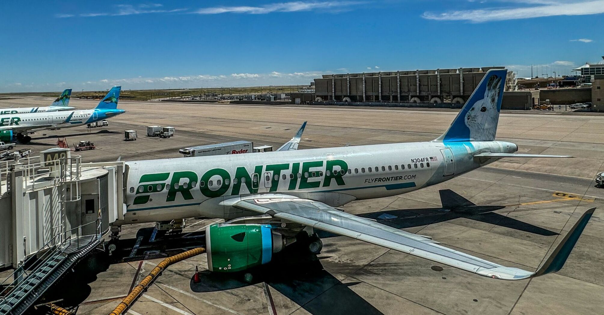 Frontier Airlines plane parked at the airport gate under a bright blue sky