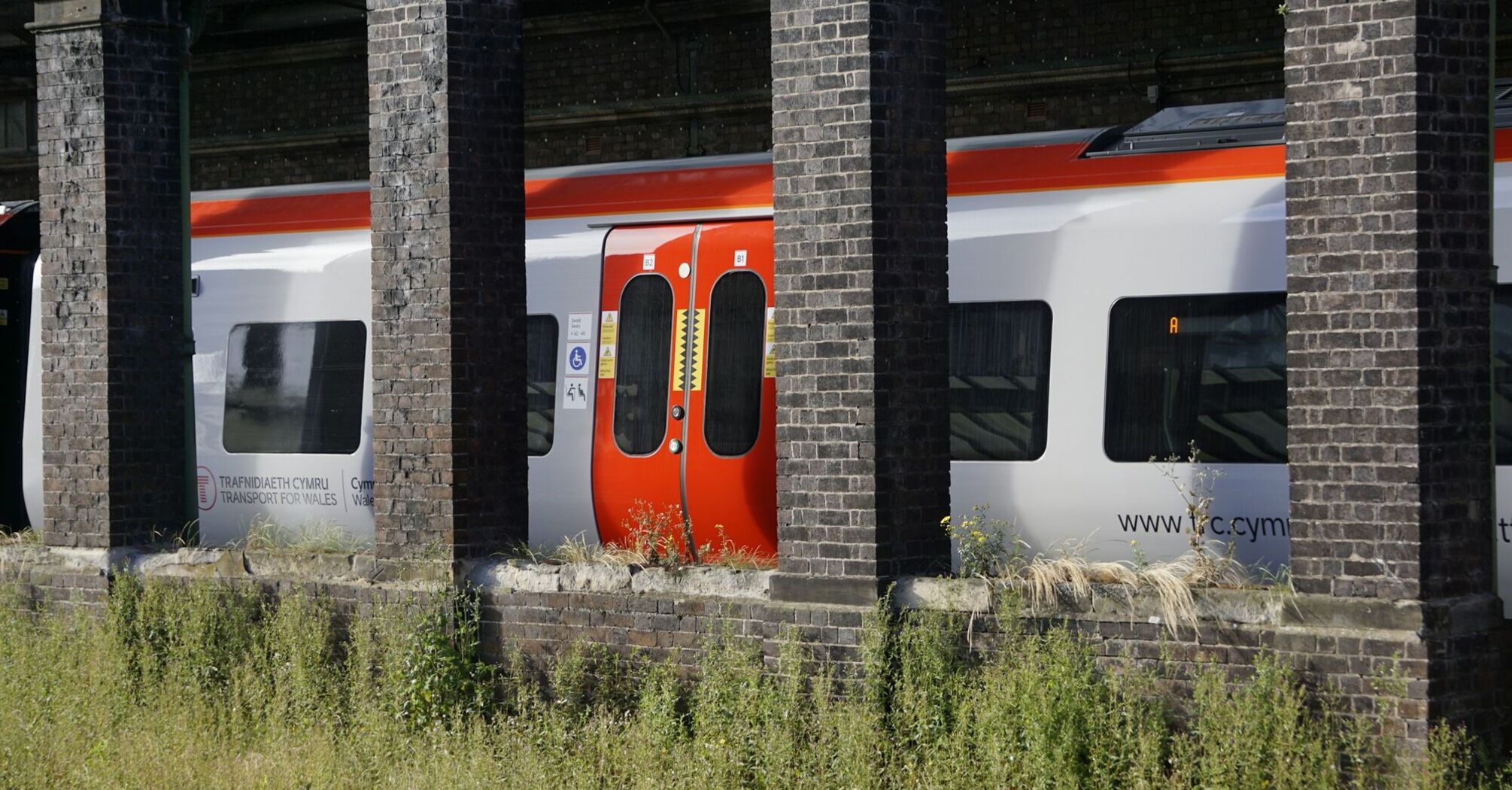 A Transport for Wales train seen through old station pillars, showcasing the new Class 756 tri-mode model