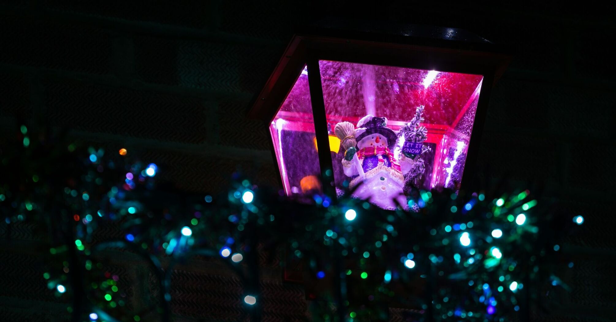 Festive snowman figurine in a lantern surrounded by glowing holiday lights