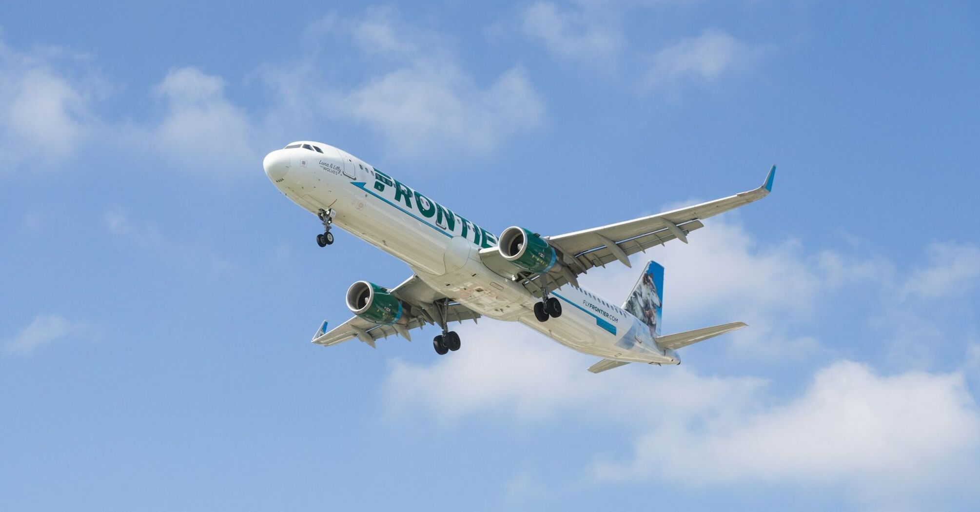 Frontier Airlines plane in mid-flight under a clear blue sky