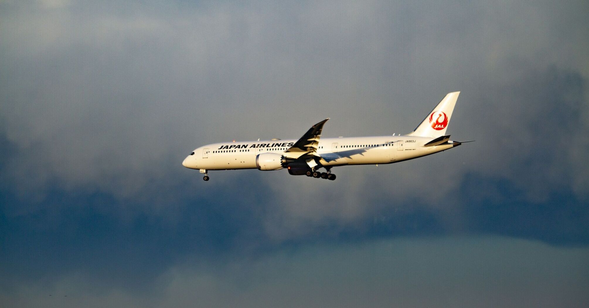 Japan Airlines aircraft approaching for landing against a cloudy sky