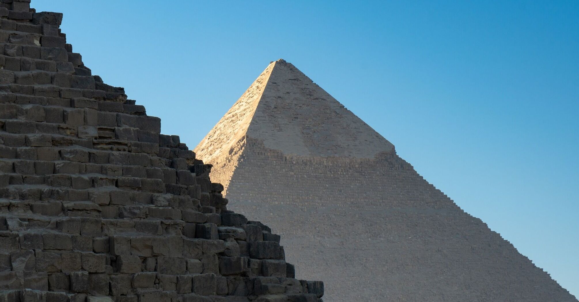 Two ancient pyramids under a clear blue sky in Giza